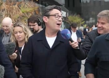 Journalists surround Andy Burnham and hold a microphone up to him as he's walking.