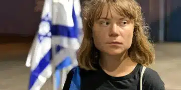 Greta Thunberg looking away, looking displeased, and behind her is an Israel flag crumpled in on itself