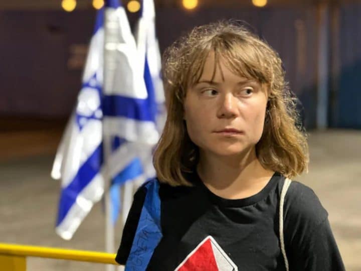Greta Thunberg looking away, looking displeased, and behind her is an Israel flag crumpled in on itself