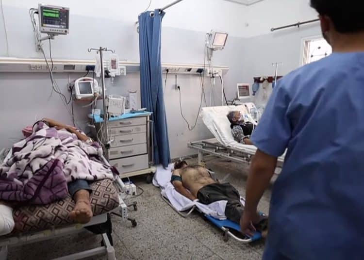Women and man in hospital beds, with one patient on the floor and a medic in scrubs walking towards them.