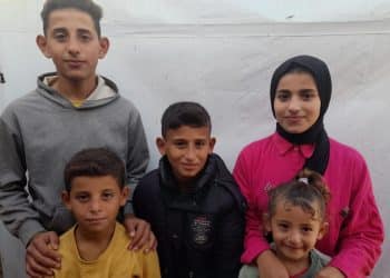 Alaa's Shamali's five children, Dima, Ibada, Salah, Abdullah, and Lina stand together in front of a displacement tent.