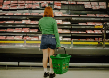 Woman stands infront of a supermarket shelf of meat holding a basket