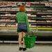 Woman stands infront of a supermarket shelf of meat holding a basket