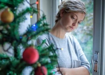 Woman standing next to Christmas tree, illustrating social isolation