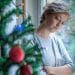 Woman standing next to Christmas tree, illustrating social isolation