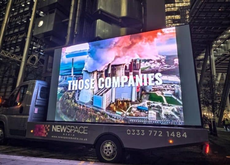 Video van against London office towers, showing spoof disaster film trailers to highlight climate impact of fossil fuel projects underwritten by insurance CEOs