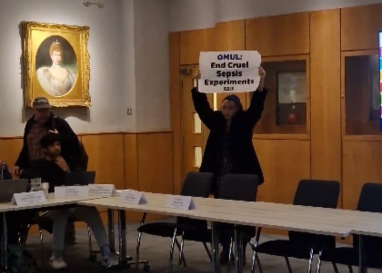 Protestor holds sign saying QMUL: End Cruel Sepsis Experiments