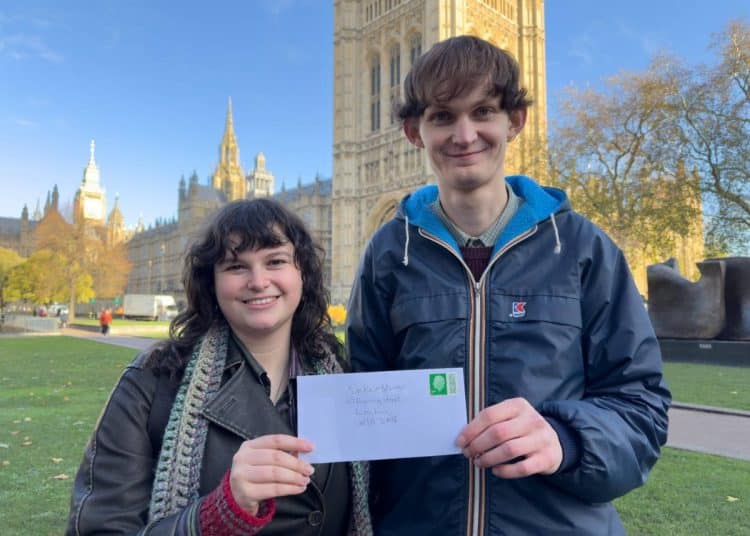 Two young people from Take Back Power standing in front of Parliament holding an envelope addressed to Keir Starmer