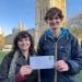 Two young people from Take Back Power standing in front of Parliament holding an envelope addressed to Keir Starmer