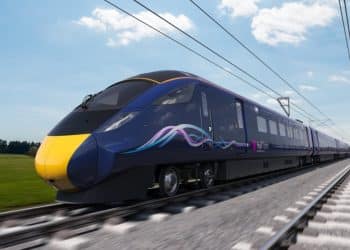 A navy blue train against a blue sky on a grey rail track