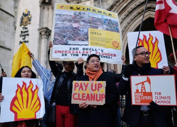 Filipino campaigners outside the Royal Courts of Justice holding signs that say Pay Up Clean Up and Make Polluters Pay For Climate Damage