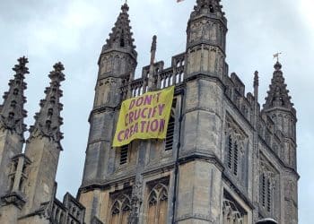 Church of England Bath Abbey with banner hanging from tower that says Don't Crucify Creation