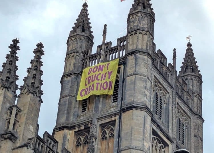 Church of England Bath Abbey with banner hanging from tower that says Don't Crucify Creation
