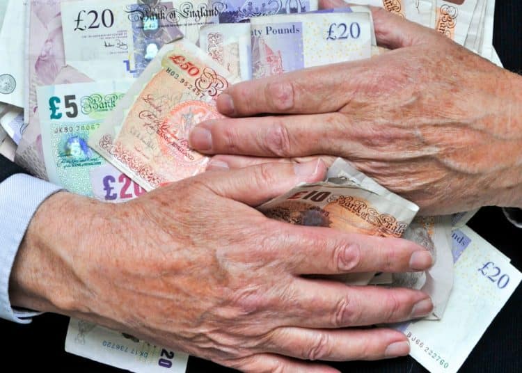 Hands holding UK bank notes to illustrate FTSE 100 CEO pay