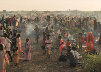 Adults and children stand and sit in the remote desert landscape of Sudan