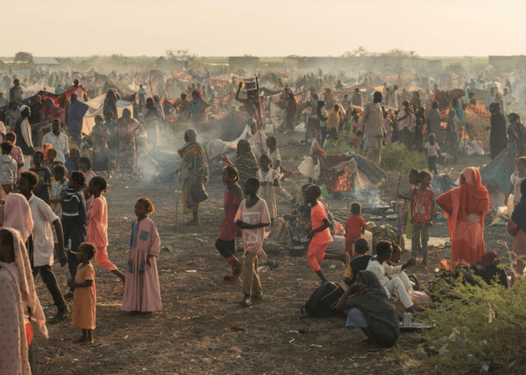 Adults and children stand and sit in the remote desert landscape of Sudan