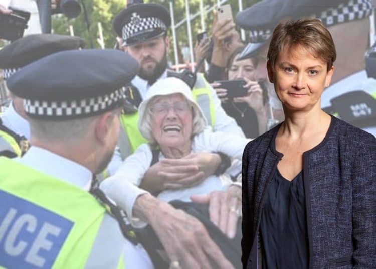 Yvette Cooper in front of an image of the police arresting an elderly protester