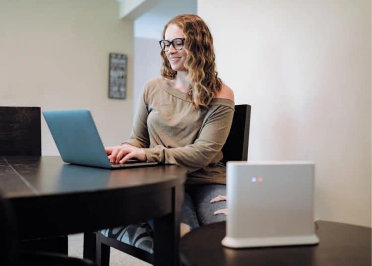 A woman working at a laptop with a broadband router in the foreground