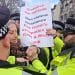 Peter Tatchell surrounded by cops and holding a placard saying Globalise The Intifada. Non-violent Resistance. End Israel's Occupation Of Gaza & West Bank