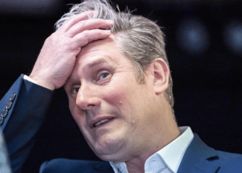Cost of living - Keir Starmer pushing back some of the hair from his forehead and looking casual in a suit without a tie and top button of his shirt undone