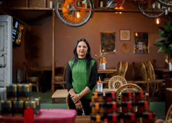 Moitra Sarkar stands in her restaurant, where ICE agents raided without reason. She's standing underneath a bicycle hanging from the ceiling and looks determined