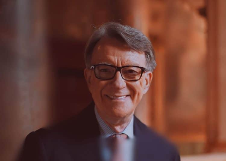 Peter Mandelson in black-rimmed glasses smiles at the camera