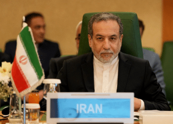 Iran foreign minister, Seyed Abbas Araghchi, sat in a chair with 'Iran' written on a plaque infront of him as though he's at a press conference or meeting