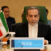 Iran foreign minister, Seyed Abbas Araghchi, sat in a chair with 'Iran' written on a plaque infront of him as though he's at a press conference or meeting