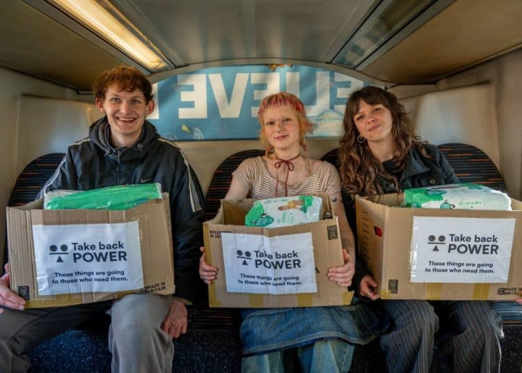 3 people take boxes of food to foodbanks. The boxes are labelled Take Back Power These Things Are Going To Those Who Need Them