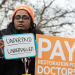 Doctors strike outside St Thomas' Hospital in London on 17 December 2025. A woman holding two placards, one says 'Underpaid, undervalued' and the other 'Pay restoration for doctors'.