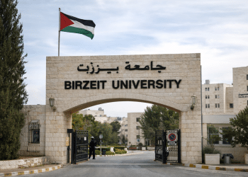 Education in Palestine: The outside of Birzeit University, where the university's name is affixed at the top of a stone archway, with a proud Palestine flag flying above