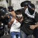 A child in Palestine, a boy, is gripped around his neck by an IOF member while blindfolded. His hands are held behind his back
