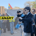 Picture of newly ratified York University Restore Britain Society members filming and jeering at student protesters. The Canary logo is on the left and in the background is an image of protesters holding up Keffiyehs to hide attendees.