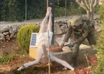 An Israeli soldier takes a sledgehammer to the face of a crucified Jesus Christ statue, which is on the ground. Taken from a BBC News report
