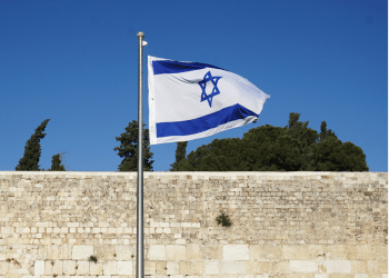 Israel's flag blows in the wind infront of a bricked wall. Israeli non-profit Shivat Zion's logo is also the Israeli flag
