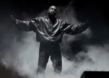 Kanye West on a stage dressed in black surrounded by smoke with his arms outstretched