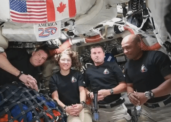 The Artemis II crew smile and look ahead while the microphone floats in the middle between the four of them