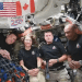 The Artemis II crew smile and look ahead while the microphone floats in the middle between the four of them