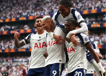 Four Tottenham Hotspur players celebrate on the pitch. One has jumped onto the other three's backs