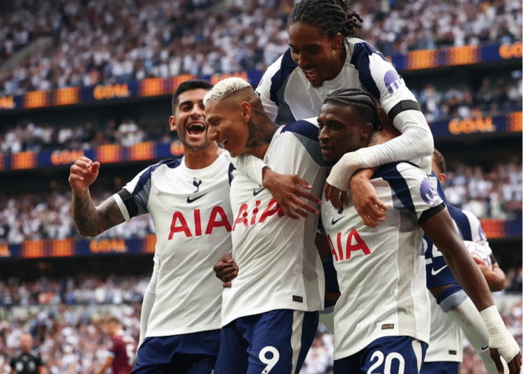 Four Tottenham Hotspur players celebrate on the pitch. One has jumped onto the other three's backs