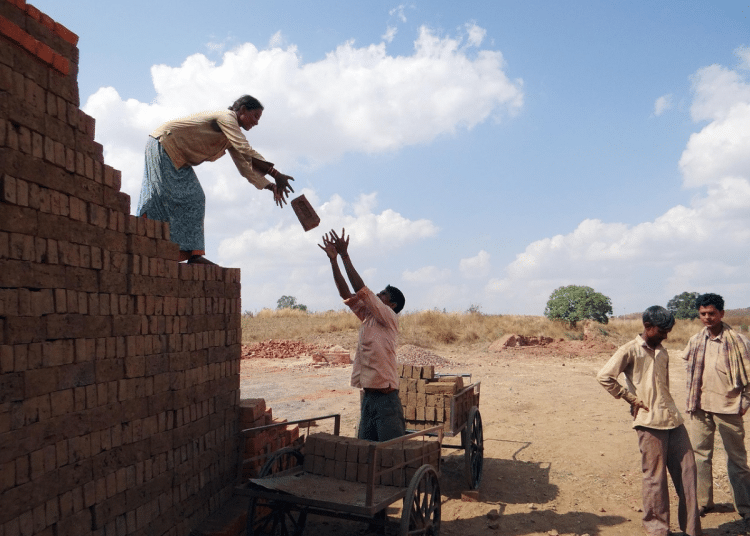 Men and women building a property in a developing country, passing each other bricks.