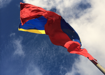 The IMF and World Bank resume dealings with Venezuela. The country's flag blows in the wind with bright blue skies above it.