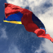 The IMF and World Bank resume dealings with Venezuela. The country's flag blows in the wind with bright blue skies above it.