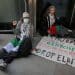 Two protesters sit, locked-on, outside the London HQ of Chubb Insurance. A banner reads: Chubb Complicit In Genocide Blood On Your Hands Drop Elbit