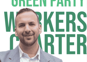 Zack Polanski smiling in front of the new Worker's Charter leaflet