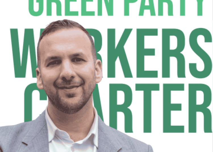 Zack Polanski smiling in front of the new Worker's Charter leaflet