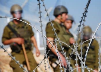 Four Israeli soldiers stand behind razor wire near the Palestinian village of Bil'in in the West Bank