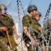 Four Israeli soldiers stand behind razor wire near the Palestinian village of Bil'in in the West Bank