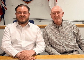 Sam Journet, wearing a white shirt with the top button undone, sat at a table smiling next to his Reform UK Basildon deputy leader, Jeff Noble. Journet is leader and an Essex County Council cabinet member