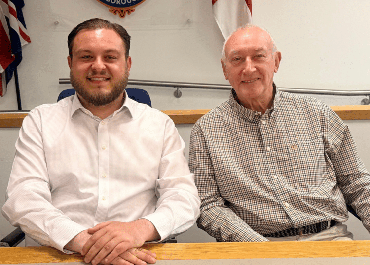 Sam Journet, wearing a white shirt with the top button undone, sat at a table smiling next to his Reform UK Basildon deputy leader, Jeff Noble. Journet is leader and an Essex County Council cabinet member